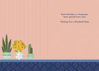 Inside of a light pink greeting card with a heartfelt message: 'Each birthday is a keepsake, more special every year. Wishing You a Wonderful Day.' Illustrated with potted plants and yellow roses along the bottom border.