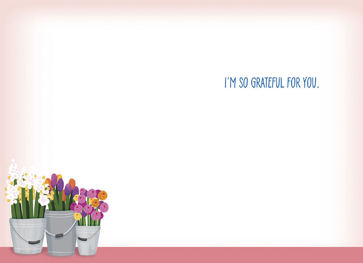 Inside view of a light pink and white thank you greeting card, showing the pre-printed message 'I'M SO GRATEFUL FOR YOU.' in blue text. A small cluster of potted flowers from the front design is visible at the bottom left, leaving ample blank space for a personalized handwritten message of appreciation.