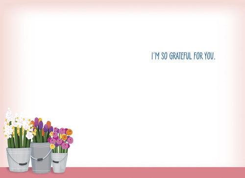 Inside view of a light pink and white thank you greeting card, showing the pre-printed message 'I'M SO GRATEFUL FOR YOU.' in blue text. A small cluster of potted flowers from the front design is visible at the bottom left, leaving ample blank space for a personalized handwritten message of appreciation.