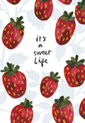 Front of a cheerful birthday greeting card featuring a vibrant, hand-drawn illustration of red strawberries scattered on a white background, with the whimsical black script text "it's a sweet Life" centered.