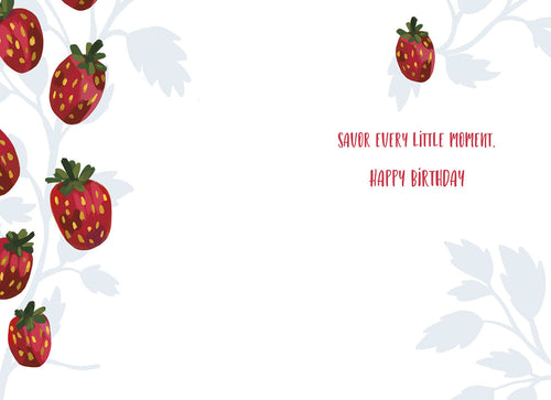 Inside of an open birthday greeting card with a clean white interior, adorned with scattered red strawberry illustrations along the left and top edges, displaying the red text "SAVOR EVERY LITTLE MOMENT. HAPPY BIRTHDAY" on the right side.