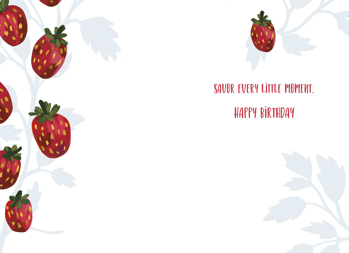 Open interior of a delightful strawberry greeting card showing scattered red strawberries and green leaves, with the heartfelt message 'savor every little moment. happy birthday' written in a charming red font on a clean white background.