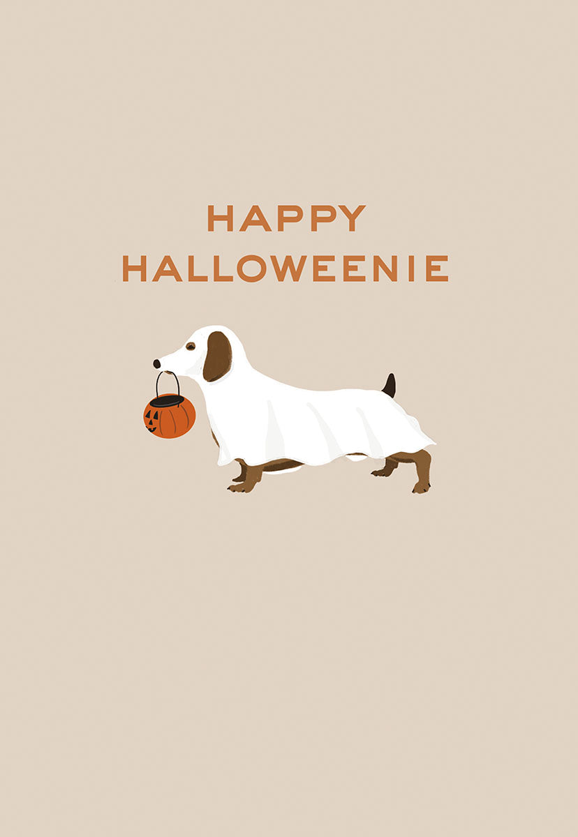 Cute dachshund dog in a white ghost costume holding an orange pumpkin candy pail, standing on a light beige background with text 'HAPPY HALLOWEENIE'. Perfect for spooky season greetings.