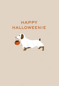 Cute dachshund dog in a white ghost costume holding an orange pumpkin candy pail, standing on a light beige background with text 'HAPPY HALLOWEENIE'. Perfect for spooky season greetings.
