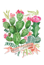 Front of a unique Christmas greeting card featuring a watercolor illustration of vibrant green prickly pear cacti with pink flowers and a banner reading "Merry Christmas" surrounded by green foliage on a white background.