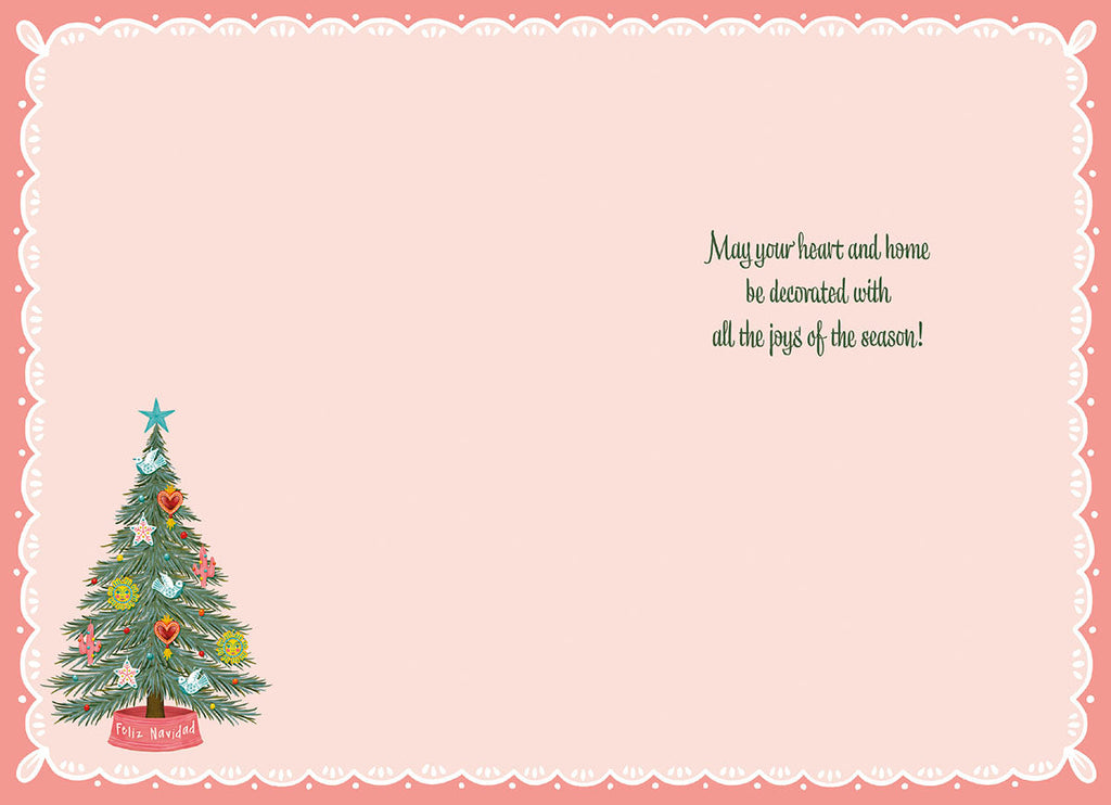 Inside of a holiday greeting card with a small decorative pine tree on the left and a warm message on the right: 'May your heart and home be decorated with all the joys of the season!'. The card has a soft pink background and a white scalloped border.