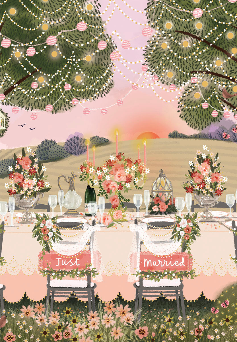 Whimsical outdoor wedding reception table at sunset with 'Just Married' chairs, floral decor, champagne, and string lights.