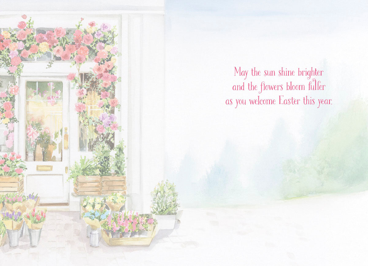 Open greeting card interior with a spring flower shop illustration on the left and a heartfelt message on the right: 'May the sun shine brighter and the flowers bloom fuller as you welcome Easter this year.' Ideal for spring season wishes.