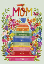 Vibrant Mother's Day greeting card featuring 'MOM' in colorful letters, a stack of storybooks, lush flowers, a bird, and a butterfly. Front message: 'I'M SO GRATEFUL THAT MY STORY BEGAN WITH YOU'.