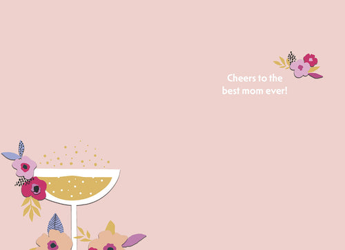 Inside of a Mother's Day greeting card with text 'Cheers to the best mom ever!' in the top right. The bottom left features a partial view of a champagne coupe glass with bubbles and colorful floral arrangements, all on a light pink background.