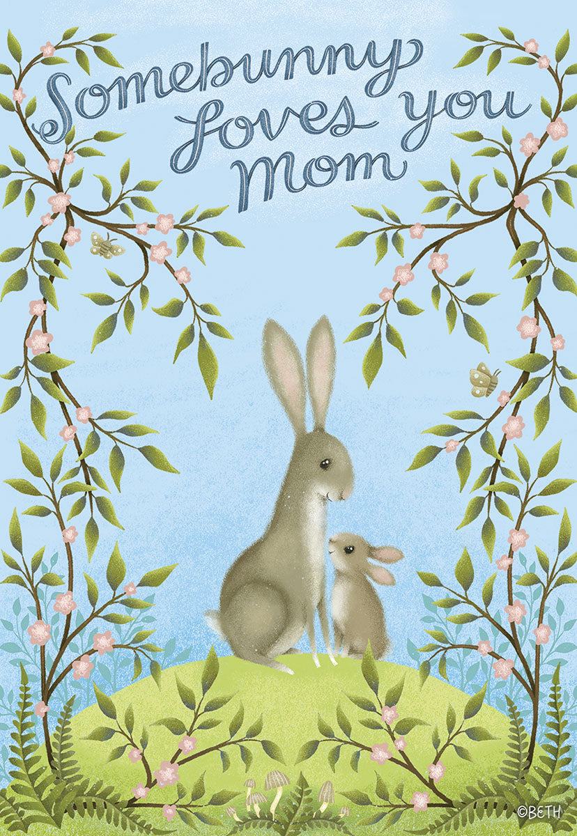 Front of a Mother's Day card with a mama bunny and baby bunny on a green hill, surrounded by flowering branches. Text reads Somebunny Loves You Mom.