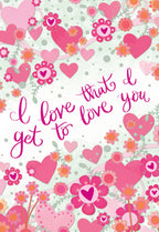 Romantic greeting card front with a pattern of pink hearts, blossoms, and green vines on a soft speckled background. Features the elegant fuchsia script 'I love that I get to love you'.