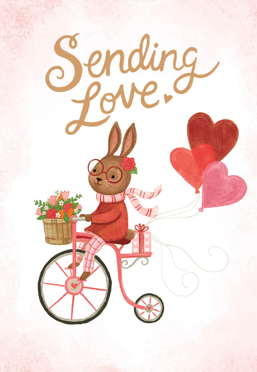 Front of a cute Valentine's Day greeting card featuring an adorable brown bunny with glasses and a scarf, riding a pink bicycle adorned with a flower basket and pulling red and pink heart balloons, with the text 'Sending Love.' against a light pink background.