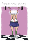 Humorous greeting card featuring an older woman with white curly hair, glasses, in a workout tank top and shorts, successfully lifting a heavy barbell above her head. The background is pink with 'Getting older makes you a hard-body.' text.