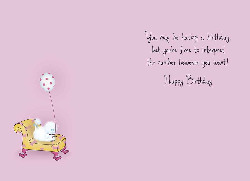 Inside of a funny birthday greeting card with a light purple background. A small fluffy white dog sits on a yellow armchair, holding a polka-dotted balloon. The text reads: 'You may be having a birthday, but you're free to interpret the number however you want! Happy Birthday.' Ideal for a lighthearted celebratory note.