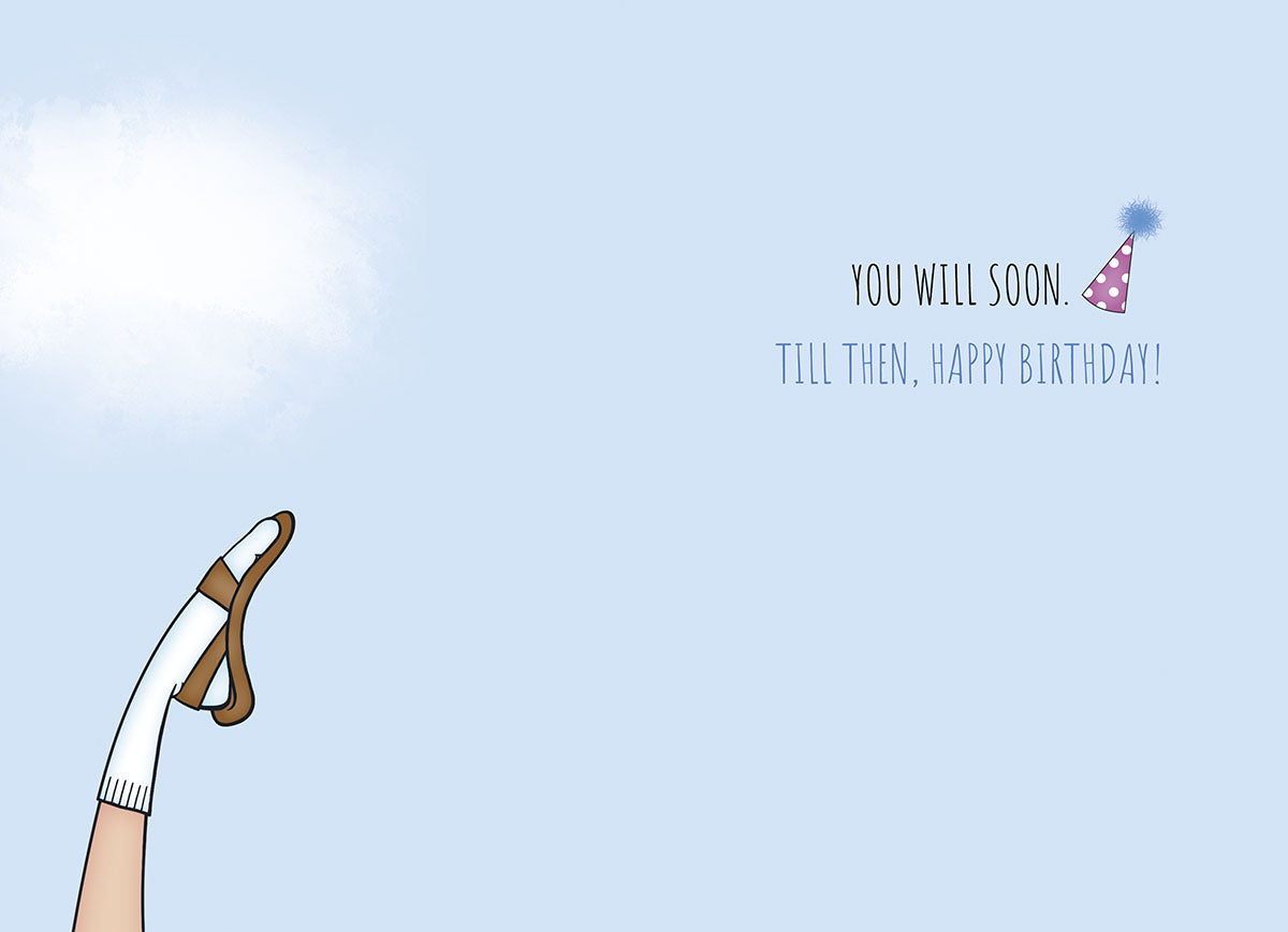 Inside view of a humorous birthday card showing a leg with a sock and sandal, a party hat, and the playful message 'YOU WILL SOON. TILL THEN, HAPPY BIRTHDAY!', ideal for an older man.