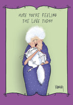 Heartfelt greeting card featuring a sweet illustration of an elderly woman with white curly hair gently hugging a fluffy white cat, set against a light green background with a whimsical purple ornate border. Text reads 'HOPE YOU'RE FEELING THE LOVE TODAY'.