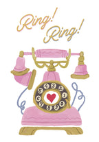 Front of a lighthearted greeting card featuring a pink vintage rotary telephone with gold accents and the words 'Ring! Ring!' in playful script. A red heart is centered on the phone dial.