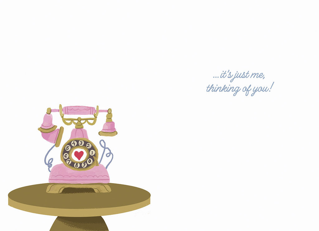 Inside view of a lighthearted greeting card featuring a small pink vintage rotary telephone on a brown table with the text '...it's just me, thinking of you!' on a white background.