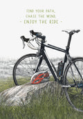 Illustrated greeting card featuring a black road bicycle leaning against a rock in a grassy field, with a red helmet beside it. Text reads: 'FIND YOUR PATH, CHASE THE WIND, - ENJOY THE RIDE -'. Ideal for him, a friend, or any cycling enthusiast.