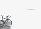 Inside of an encouraging greeting card, showing a faint illustration of a bicycle in the lower left corner and 'HAPPY BIRTHDAY' text in green on the right, on a light grey background.