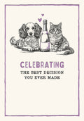 Front of a cute anniversary greeting card featuring a black and white sketch illustration of a fluffy dog and a tabby cat sitting next to a champagne bottle with two purple hearts. The text reads: 'CELEBRATING THE BEST DECISION YOU EVER MADE'.