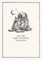 Front of an encouragement greeting card for her, featuring a hand-drawn illustration of a golden retriever dog and a tabby cat sitting together under a crescent moon and stars, with the comforting text 'some days might feel heavier than others' in blue script. The card has a soft cream background and a subtle blue border, conveying a heartfelt, supportive, and peaceful sentiment for a friend.