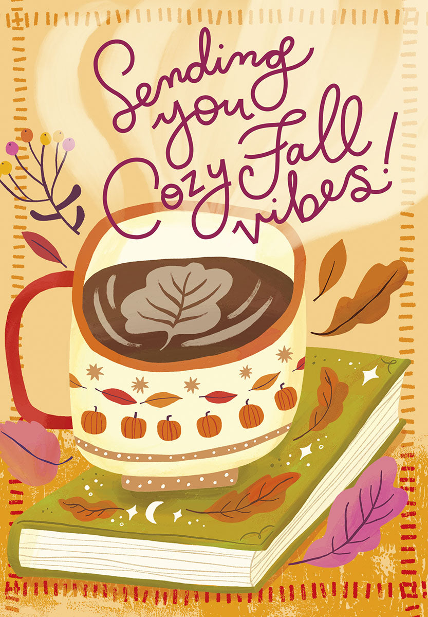 Cozy fall greeting card front featuring a warm mug of hot cocoa with leaf latte art, resting on an autumn-themed book, surrounded by fall leaves and the text 'Sending you Cozy Fall Vibes!'. Perfect for friends celebrating harvest season or leading up to a festive October.