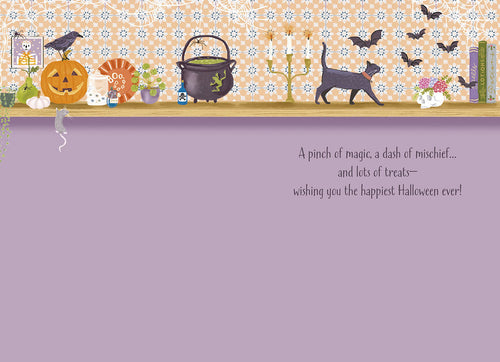 Inside of a cute Halloween greeting card revealing a purple blank space for a personal message and pre-printed text: 'A pinch of magic, a dash of mischief... and lots of treats— wishing you the happiest Halloween ever!', surrounded by top shelf decorations including a black cat and cauldron.