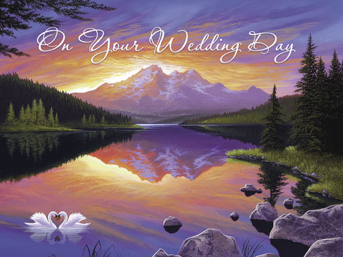 Front of a heartfelt wedding greeting card featuring two white swans forming a heart shape on a serene lake, reflecting a vibrant sunset over majestic mountains and evergreen trees, with the text 'On Your Wedding Day' elegantly scripted.