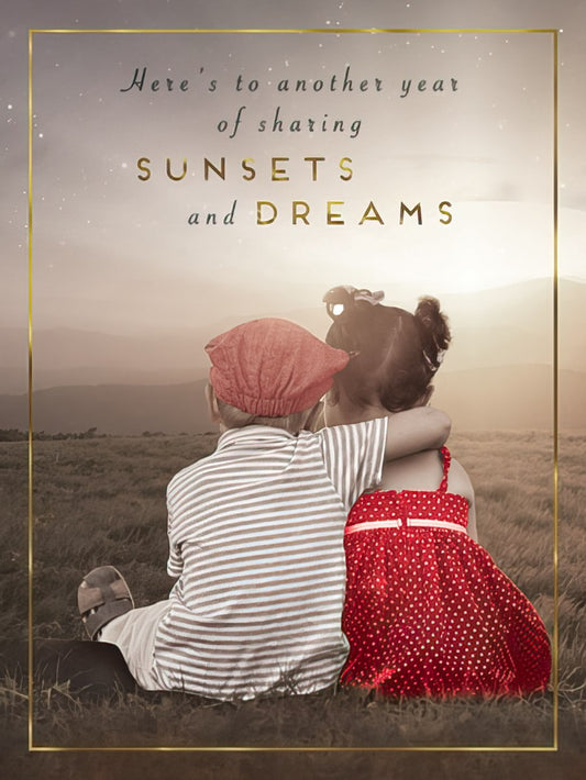Anniversary card featuring two young children sitting in a field, gazing at a golden sunset, with elegant gold foil text. The scene symbolizes shared dreams and a future together.