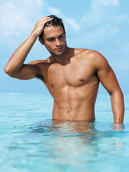 Handsome man, shirtless, in clear blue ocean water, hand running through wet dark hair, looking thoughtful. Beach birthday card image.