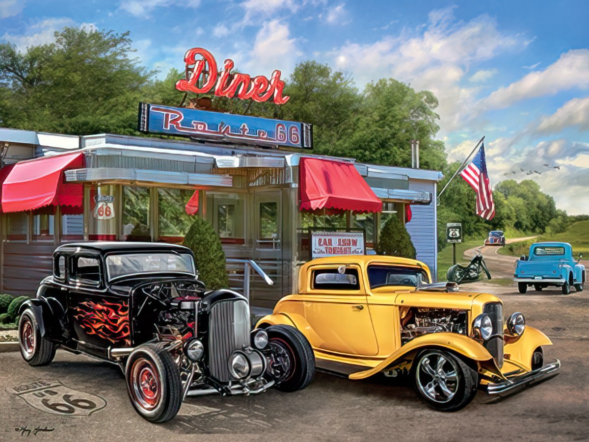 Two classic hot rods, a black one with flames and a yellow one, parked in front of a retro Route 66 diner under a cloudy sky.