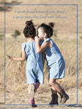 Two young girls in denim rompers and cowboy boots whispering secrets outdoors in a rustic field, symbolizing close friendship and shared stories.