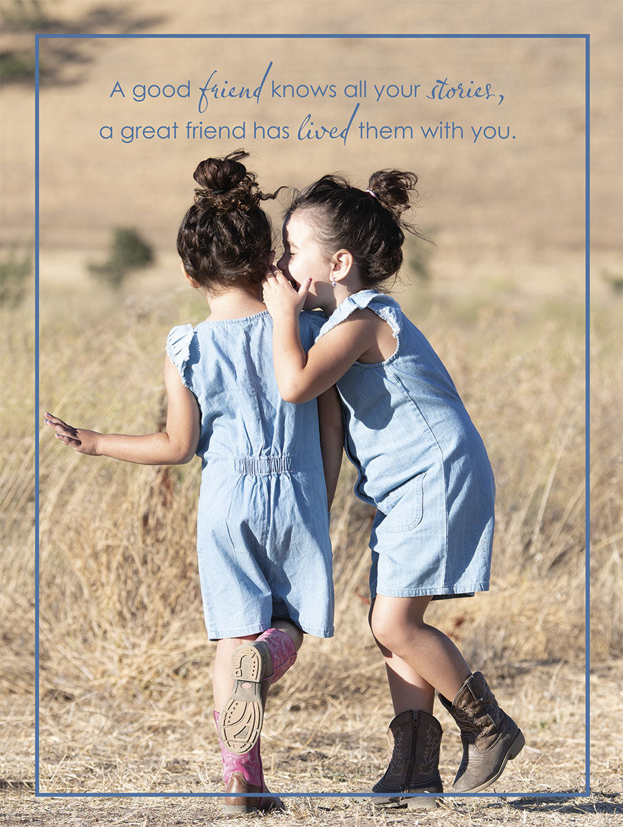 Two young girls in denim rompers and cowboy boots whispering secrets outdoors in a rustic field, symbolizing close friendship and shared stories.