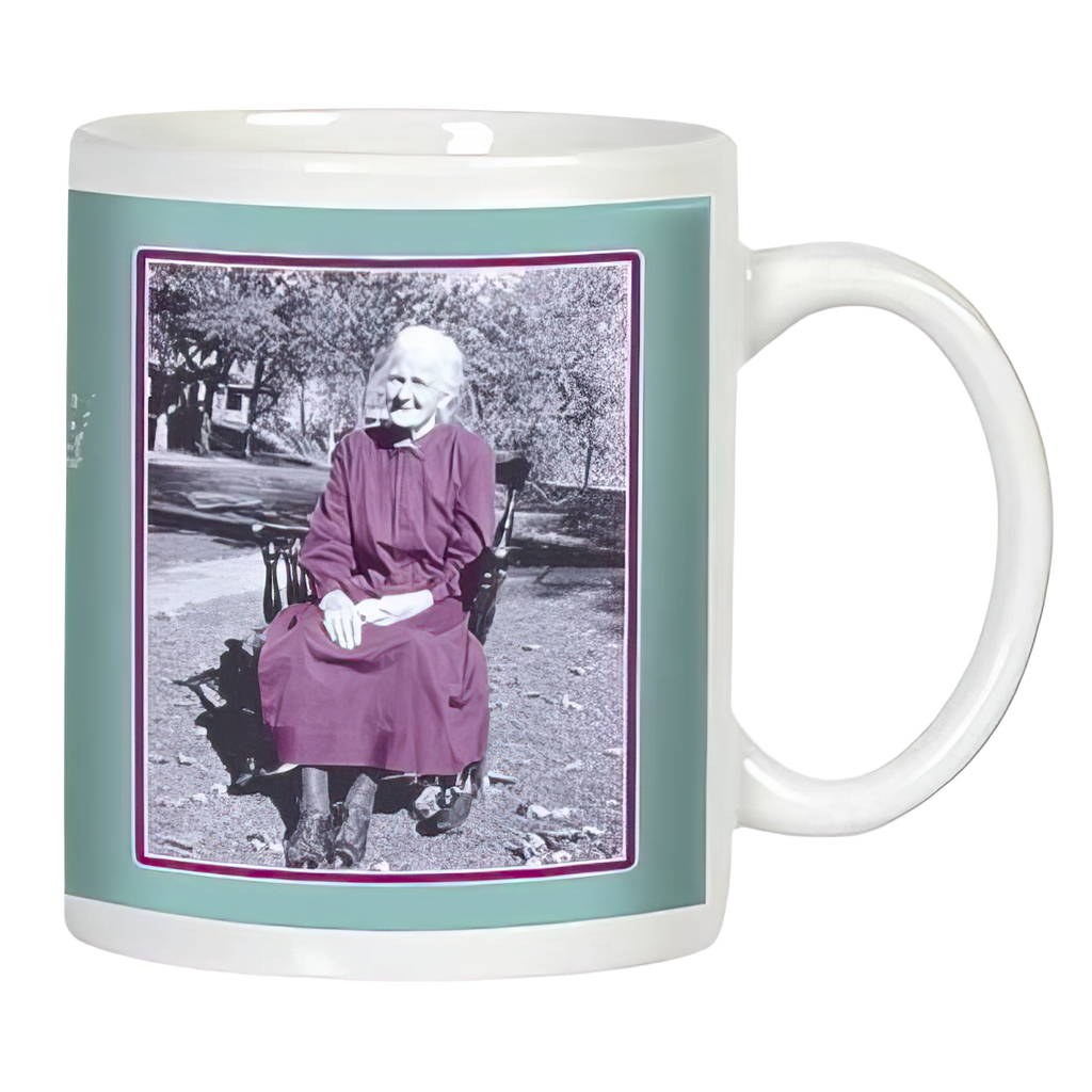 White ceramic mug featuring a vintage-style black and white photo of a smiling elderly woman in a dress sitting outdoors, framed by a teal border.