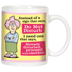 Sassy white ceramic mug featuring a cartoon of a grumpy woman with pink hair and glasses, arms crossed. Text reads: 'Instead of a sign that says, Do Not Disturb I need one that says, Already disturbed, proceed with caution.' Perfect funny gift.