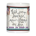 Side view of a white ceramic mug showcasing the inspirational quote 'With every sunrise new dreams are born' in elegant script font, flanked by colorful feathers, all against a textured white wood-grain background with tribal borders.