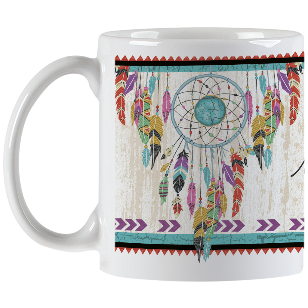 White ceramic mug displaying a beautiful dreamcatcher graphic with multi-colored feathers and a central turquoise stone, beside part of the inspiring 'new dreams are born' quote.
