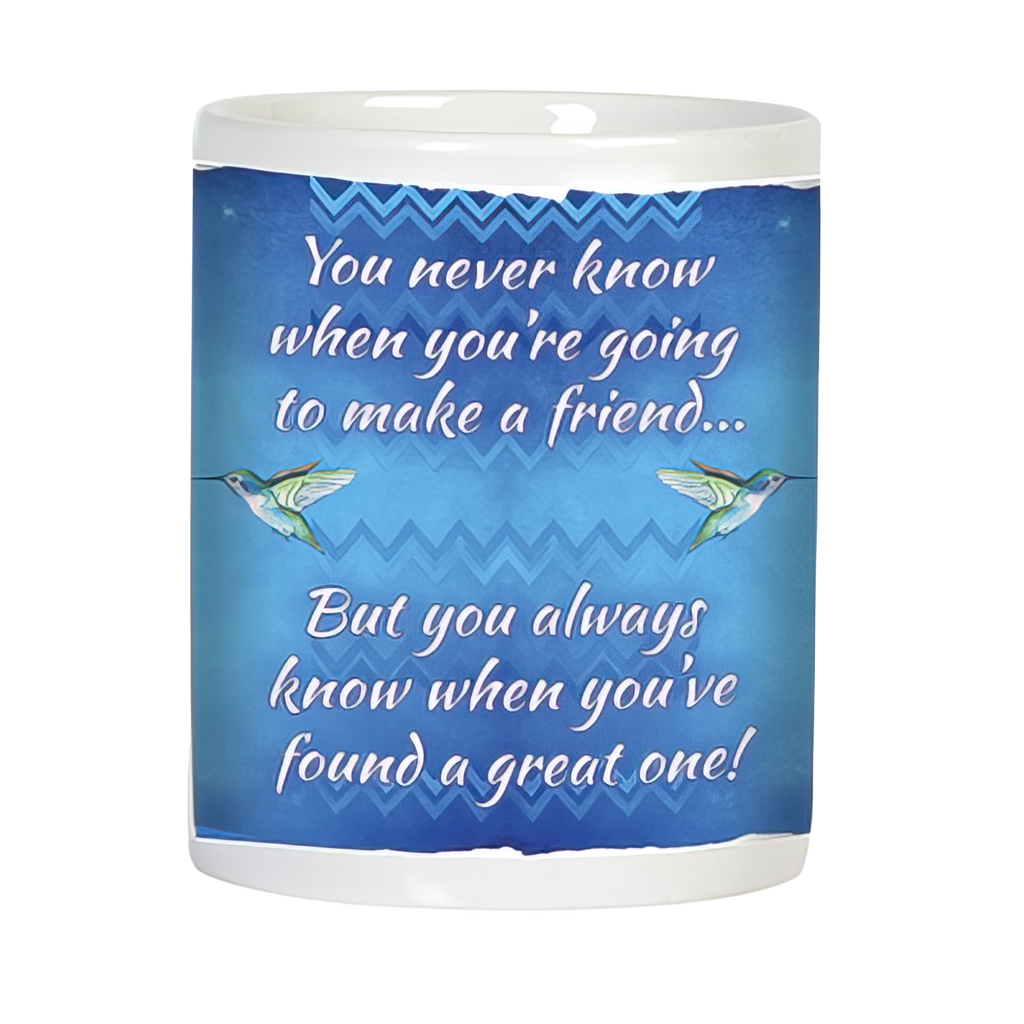Back view of a white ceramic mug with a heartfelt friendship quote in white script: 'You never know when you're going to make a friend... But you always know when you've found a great one!' accompanied by two green hummingbirds on a blue patterned backdrop.
