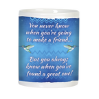 Back view of a white ceramic mug with a heartfelt friendship quote in white script: 'You never know when you're going to make a friend... But you always know when you've found a great one!' accompanied by two green hummingbirds on a blue patterned backdrop.