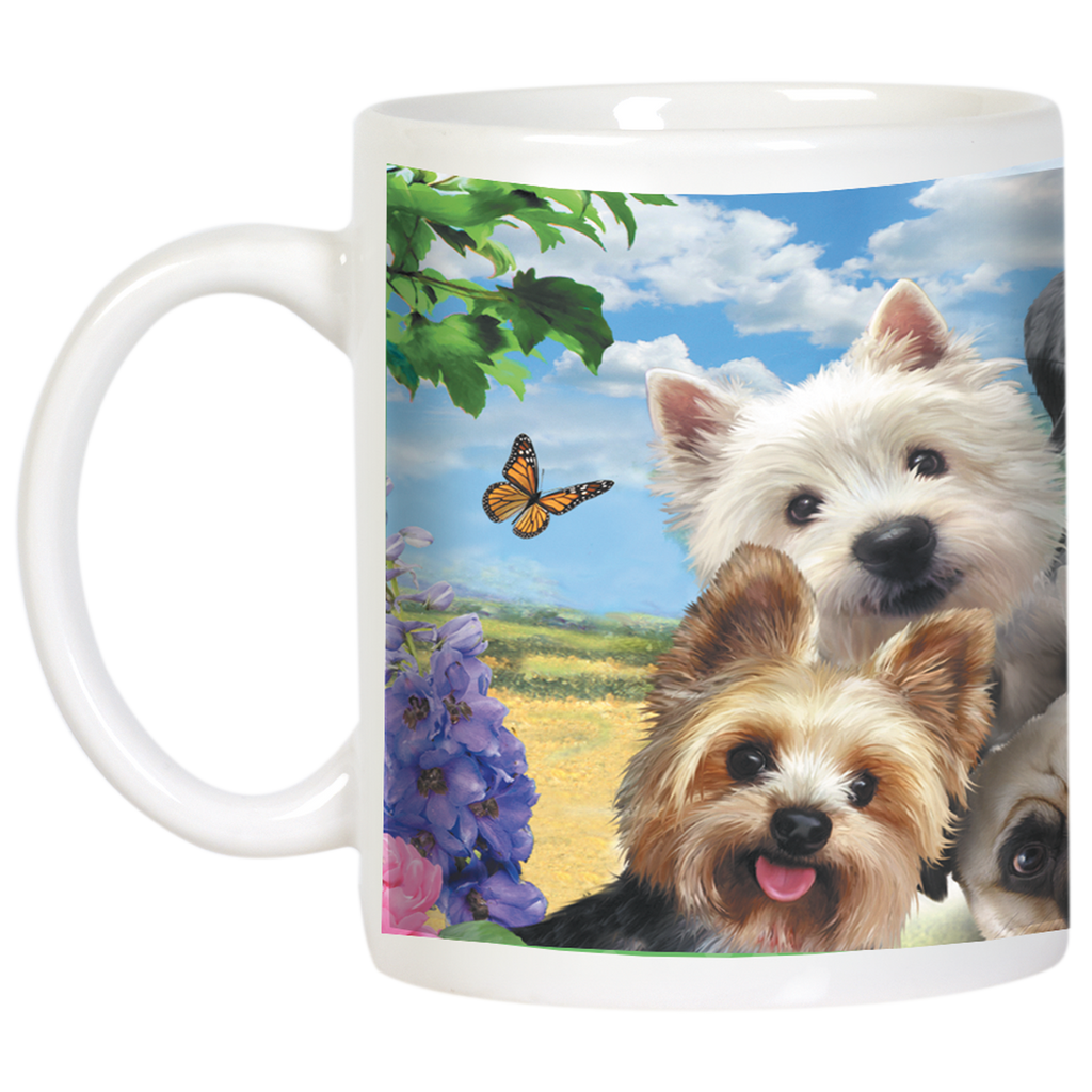 Close-up of a white dog-themed mug displaying a Westie, Yorkshire Terrier, and Pug smiling, with purple flowers and a butterfly in a sunny field backdrop.