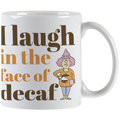 Close-up front view of a white ceramic coffee mug with the slogan 'I laugh in the face of decaf' in brown and orange text, featuring a sassy cartoon woman holding a coffee pot.