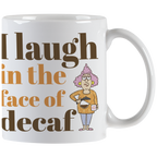 Close-up front view of a white ceramic coffee mug with the slogan 'I laugh in the face of decaf' in brown and orange text, featuring a sassy cartoon woman holding a coffee pot.
