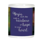 Side view of white ceramic mug displaying an inspirational quote 'Begin each day with a rainbow of hope in your heart' on a deep purple background.