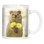 White ceramic coffee mug featuring a smiling quokka holding two cheerful yellow daisy-like flowers on a bright, blurry background.