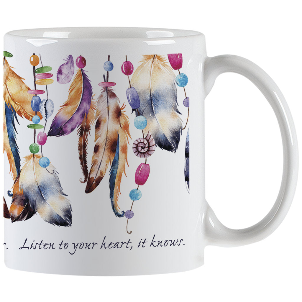 Close-up of a white ceramic mug, showing the right side with a handle. The mug features a vibrant design of hanging feathers in various earthy and pastel colors, interspersed with colorful beads. Part of the quote 'Listen to your heart, it knows.' is visible in elegant script below the design.