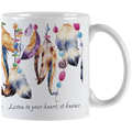 Close-up of a white ceramic mug, showing the right side with a handle. The mug features a vibrant design of hanging feathers in various earthy and pastel colors, interspersed with colorful beads. Part of the quote 'Listen to your heart, it knows.' is visible in elegant script below the design.