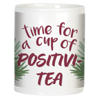 Side view of a white ceramic mug with the encouraging quote 'time for a cup of POSITIVI-TEA' in elegant maroon script, framed by green leafy accents, promoting positivity with every sip.