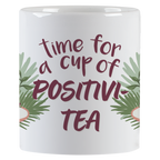Side view of a ceramic mug with green leaf accents and the inspiring text 'time for a cup of POSITIVI-TEA' in purple script.